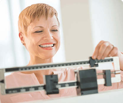 A woman smiles as she stands on the scale.