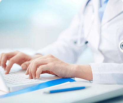 A person in white lab coat typing on a laptop.