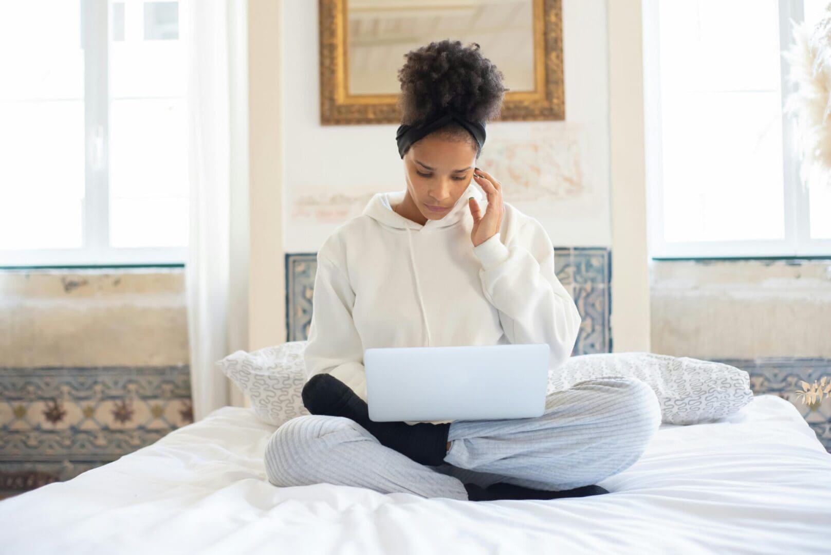A woman sitting on the bed looking at her laptop.