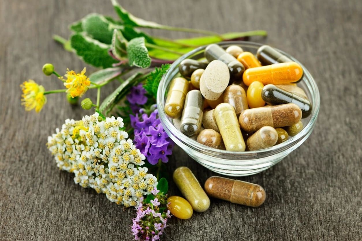 A bowl of pills and flowers on the table.