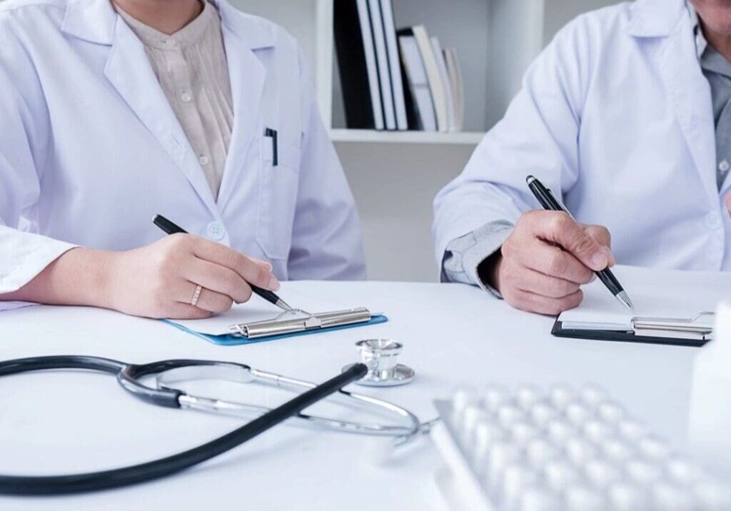 Two doctors are sitting at a table with stethoscopes around their necks.