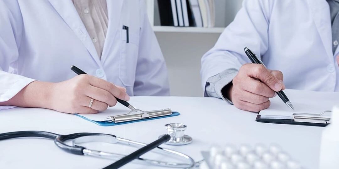 Two doctors are sitting at a table with stethoscopes around their necks.